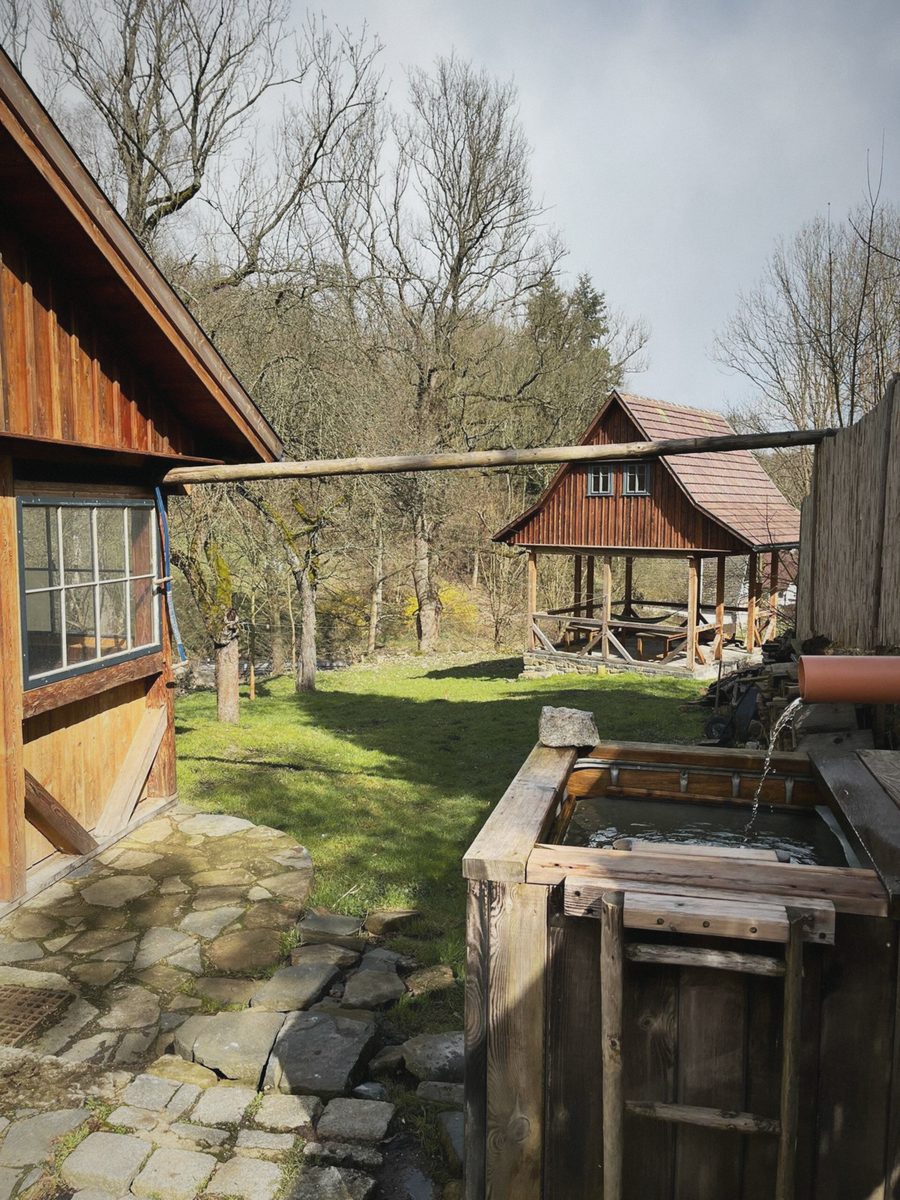 Dřevěná káď u domu, v pozadí altán a stromy