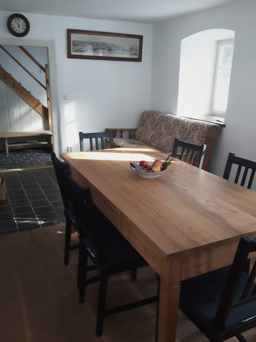 Dlouhý dřevěný stůl s tmavými židlemi a mísou ovoce